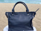 Sapphire leather satchel bag back view on a sandy beach with ocean in the background