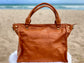 Whisky Brown leather satchel bag back view on a sandy beach with ocean in the background