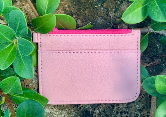  Light Pink pouch back view with a bright pink zipper on a stone surface surrounded by green leaves