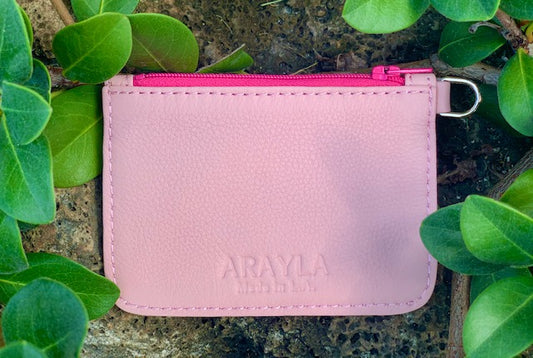 Light Pink pouch front view with a bright pink zipper on a stone surface surrounded by green leaves
