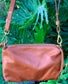 Whisky brown butter leather bag back view with a strap against a green leafy background