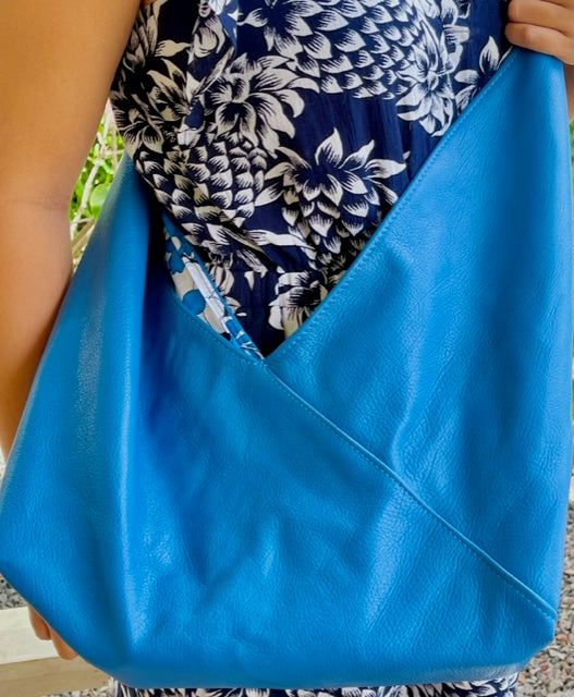 Cobalt Blue leather hobo bag with the strap tied is held by a person across her body.