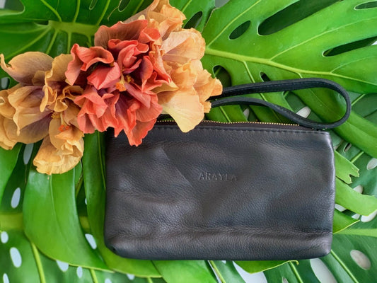 Mini Clutch In Onyx Butter Leather With Python Embossed Calfskin Wrist Strap on a green leaf background