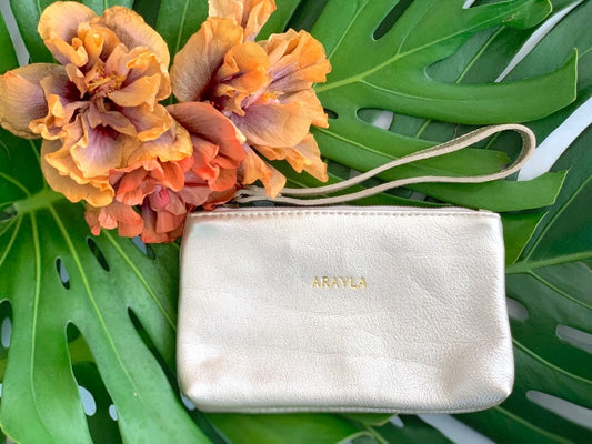 Mini Clutch In Pale Gold Metallic Butter Leather on a green leaf background