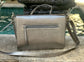 Pewter Metallic leather bag on a stone surface with a blurred fountain in the background.