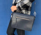 A woman holding a sapphire leather bag on her shoulder against a blue background