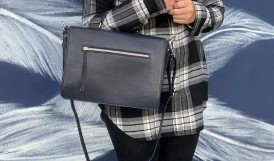 A woman holding a sapphire leather handbag in the crook of her hand against a blue textured background