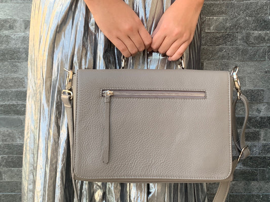 A woman holding a warm grey silky textured leather bag against a brick wall background