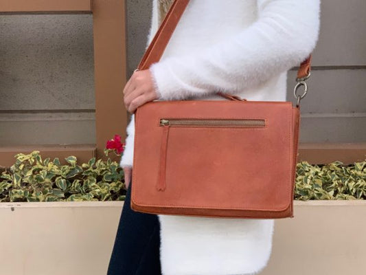 A whisky Brown leather bag held by a woman on her shoulder who's wearing a white fur coat.