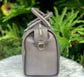 Titanium gray leather bag side view with a silver zipper on a white surface with green foliage in the background