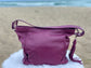 An aubergine hobo bag back view on a white surface with a beach background