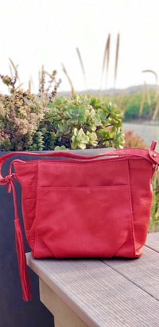A scarlet red butter leather bag with a tassel on a wooden table with a blurred natural background