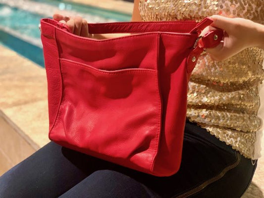 A woman wearing sparkly top and holding a scarlet red bag with a pool  in the background