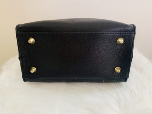 Close-up of the bottom of the onyx black leather bag featuring four gold protective metal feet, displayed on a white faux fur surface.