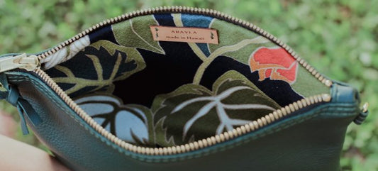 Close-up of the mini leather pouch  interior with a visible brand logo on a Hawaiian barkcloth lining, key leash, zip pocket, and two slip mobile pockets.
