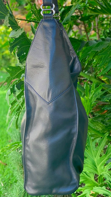 Sapphire leather hobo bag side view hanging on a tree branch with green leaves in the background