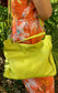 A woman wearing a bright orange floral dress with the tahitian lime bag on the shoulder using the bag long strap.