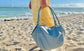 A woman holding a light grey handbag on a sandy beach with ocean in the background