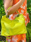 A woman holding the tahitian lime bag in the crook of her arm with a floral dress in the background