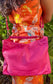 Woman wearing a bright orange floral dress with a pink crossbody bag against a green leafy background